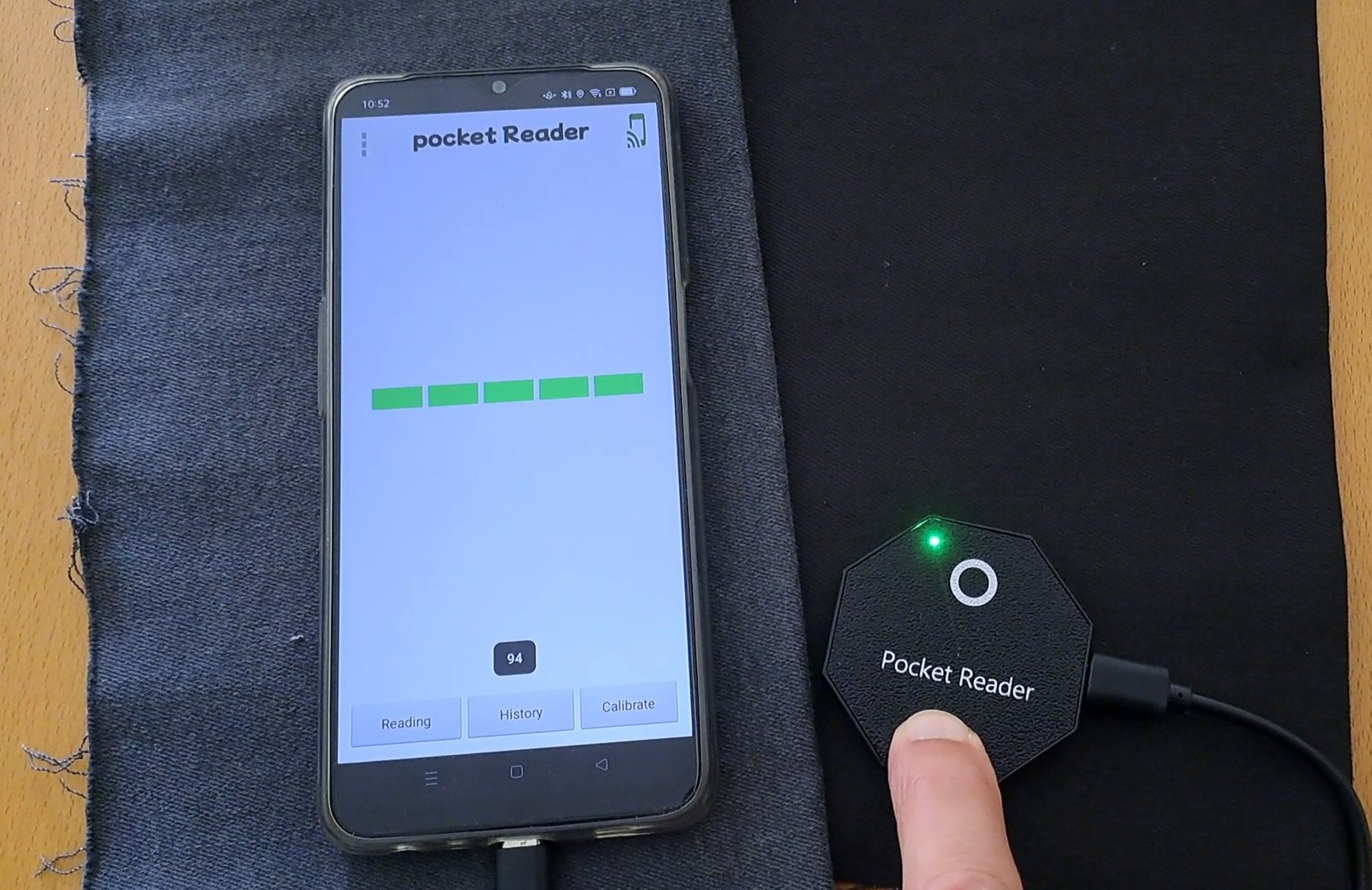 The Pocket Reader: a compact octagonal reader with a green status LED, connected by USB-C to an Android phone running the Pocket Reader app mid-reading.